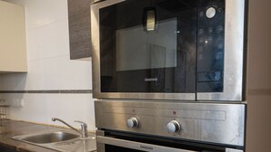 A kitchen with a built-in microwave, oven, and stainless steel sink. - Kilua Residences by Cityblue (Mombasa)