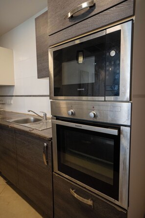 A kitchen with a built-in microwave, oven, and stainless steel sink. - Kilua Residences by Cityblue (Mombasa)