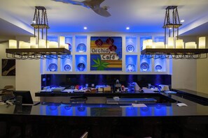A bar area with a sign reading 'Orchid Café,' a ceiling fan, and a modern light fixture. - Kilua Residences by Cityblue (Mombasa)