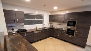A modern kitchen with dark wood cabinets, stainless steel appliances, and a granite countertop. - Kilua Residences by Cityblue (Mombasa)