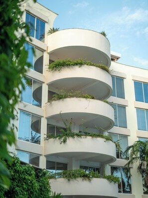 Un edificio de varios pisos con balcones, ventanas amplias y vegetación.