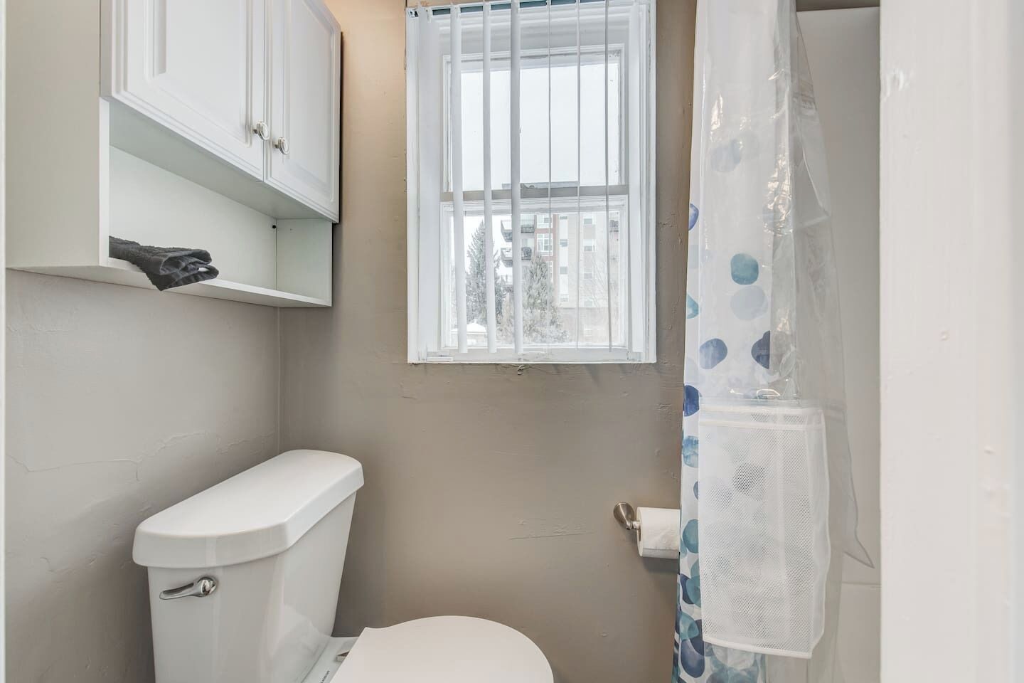 A small bathroom with a toilet, a window, and a shower curtain.