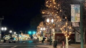 Une rue bordée d’arbres décorés de guirlandes lumineuses, un panneau indiquant l’entrée de la vieille ville d’Arvada, et un lampadaire vert.