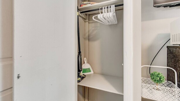 Une armoire blanche avec une tringle pour suspendre les vêtements, une étagère ornée d’une plante verte et une chaise blanche également agrémentée d’une plante verte.