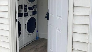 Une buanderie équipée de deux machines à laver et de deux sèche-linge à chargement frontal, superposés, avec une porte et un petit paillasson à l’entrée.