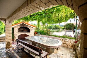 An outdoor patio with a stone fireplace, a round table, and a bench. - Studio apartment in Lopar with Air condition, WIFI (4886-5) (Lopar)