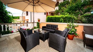 Een terras met rieten meubels, een tafel en een grote parasol.