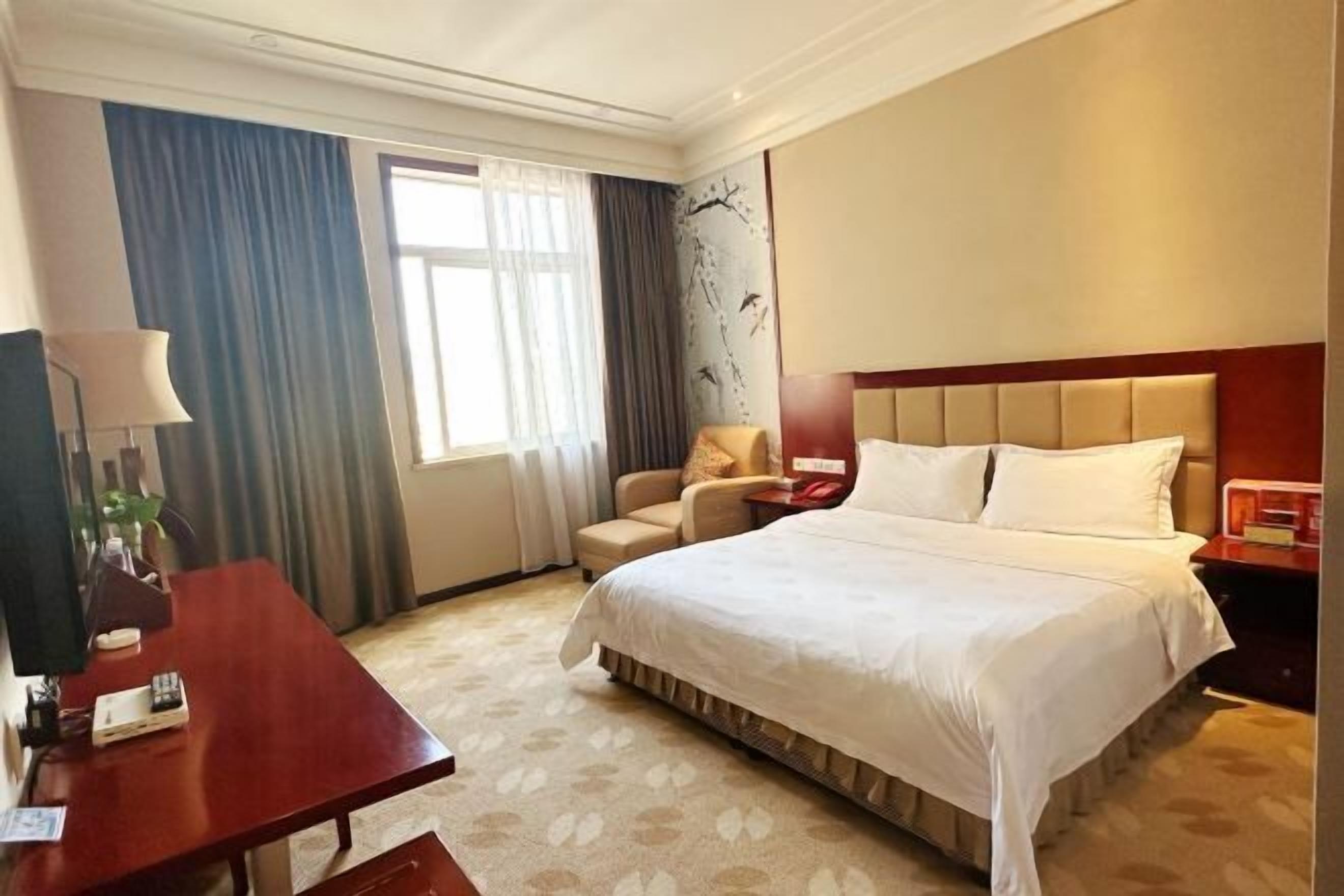 Habitación de hotel con una cama grande, un escritorio, una silla y una ventana con cortinas.