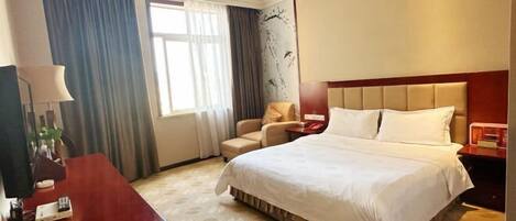Habitación de hotel con una cama grande, un escritorio, una silla y una ventana con cortinas.