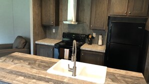 A kitchen with dark wooden cabinets, a black stove, a stainless steel sink, and a black refrigerator. - Relax, Enjoy, Explore, On Cane! (Natchez)