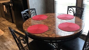 A round wooden table with four red placemats, surrounded by black chairs with ornate metalwork. - Relax, Enjoy, Explore, On Cane! (Natchez)