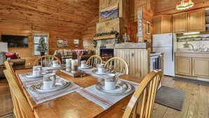A cozy cabin interior with a dining table set for four, a fireplace, wooden walls, and a kitchen area. - 4.3 miles to BR center, Private, Family Fun, Hot Tub, Serene  (Blue Ridge)