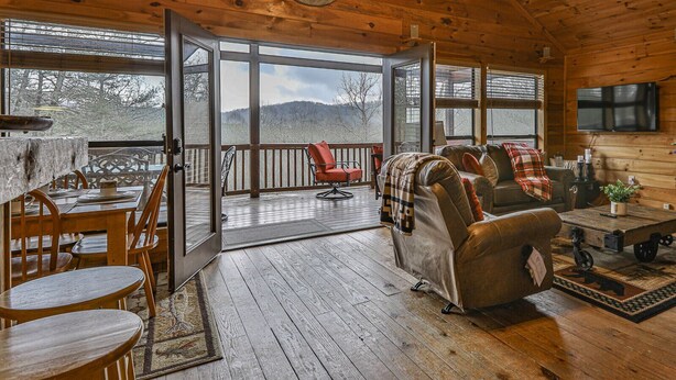 A cozy cabin interior with a dining area, a sofa, and a TV. - 4.3 miles to BR center, Private, Family Fun, Hot Tub, Serene  (Blue Ridge)