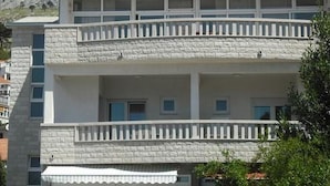 Un edificio de dos pisos con balcones, fachada de piedra y montañas al fondo.