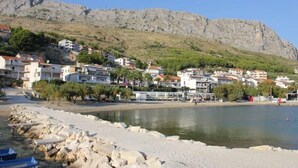 Un pueblo costero con edificios a lo largo del paseo marítimo, una playa rocosa y una montaña en el fondo.
