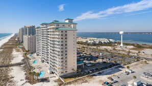 A beachfront hotel with multiple floors, a parking lot, and a view of the ocean.