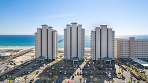 A high-rise hotel with multiple floors, a parking lot, and a beach view.