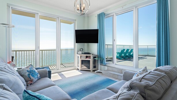 A living room with a large sofa, a flat-screen TV, and a view of the ocean through large windows.