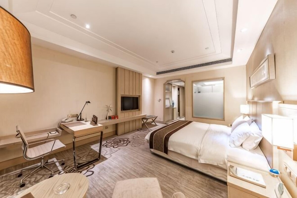 A hotel room with a bed, desk, chair, TV, and a mirror.