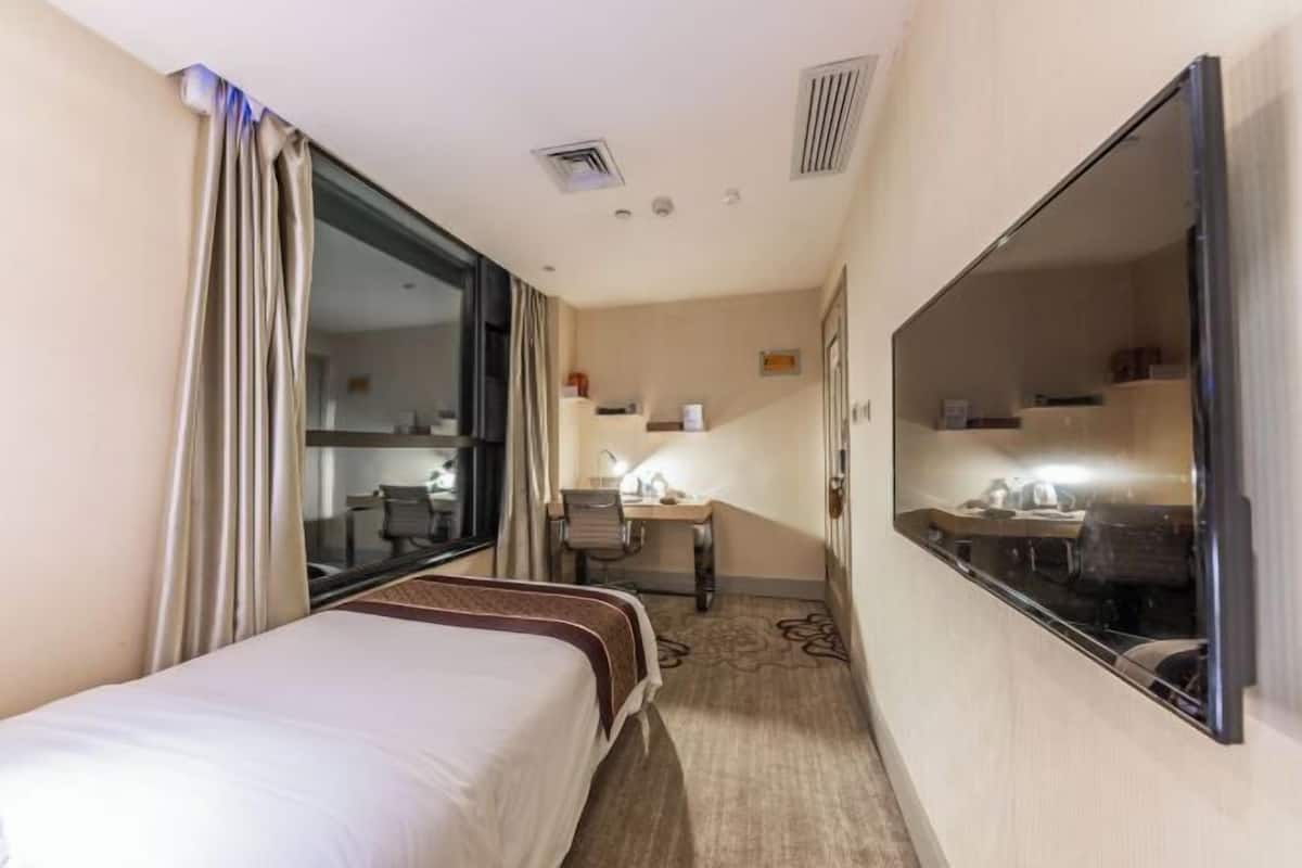 Ett hotellrum med en säng, ett skrivbord, en stol, en tv och ett fönster med gardiner.
