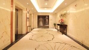 A hotel corridor with marble walls, a patterned carpet, and a reception desk with a potted plant.