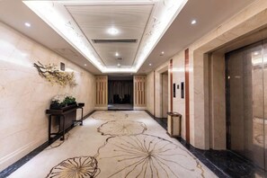 Un pasillo de hotel con piso de mármol, una recepción y un ascensor.