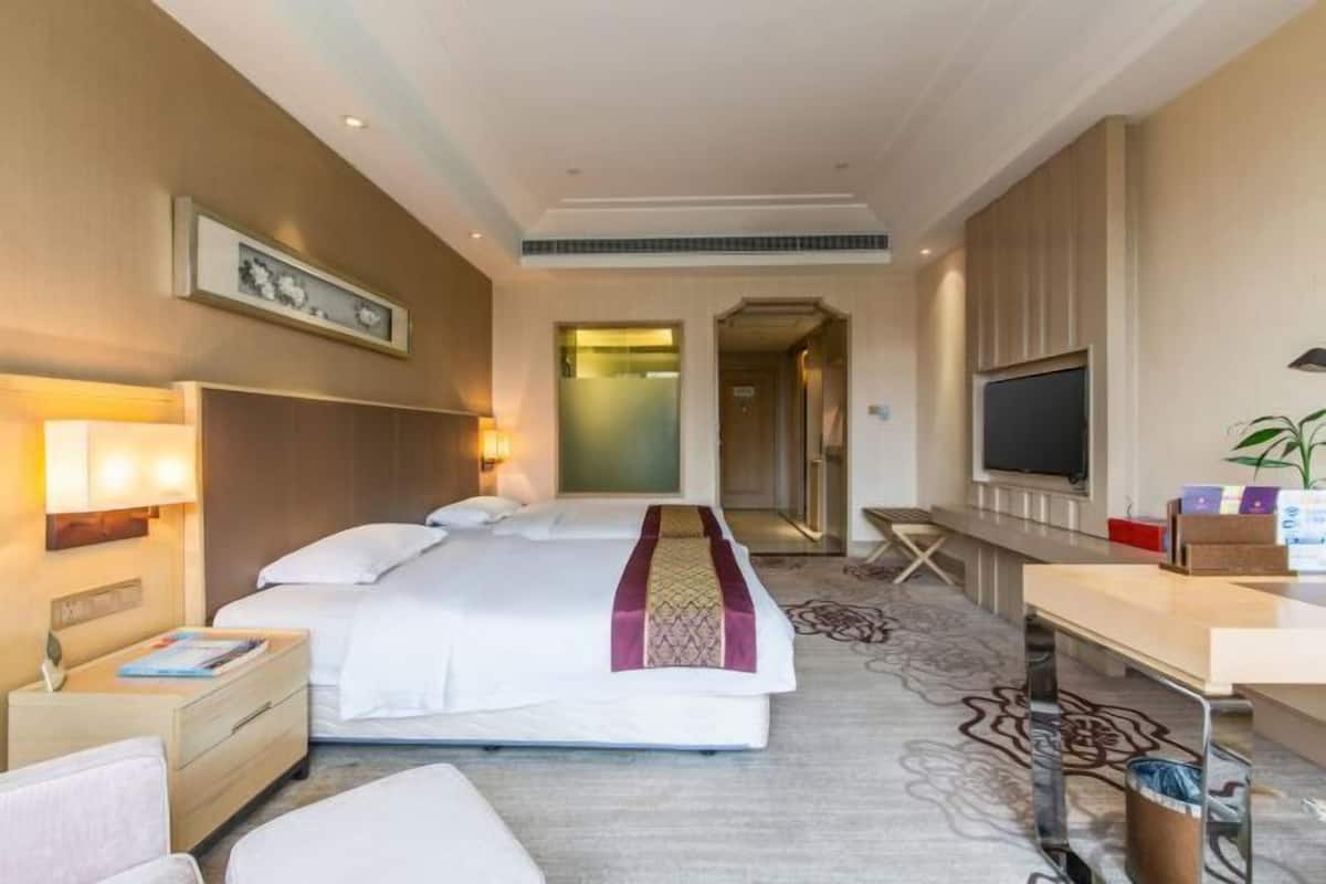 Ett hotellrum med en säng, ett nattduksbord, en lampa, en tv, ett skrivbord, en stol och en spegel.