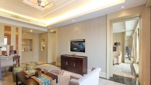 A modern hotel room with a flat-screen TV, a sofa, a dining table, and a large mirror. - Xili International Hotel (Hong'an)