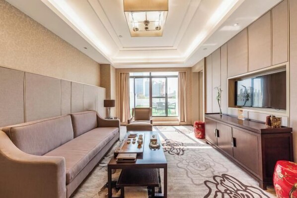 Une chambre d’hôtel moderne, dotée d’un canapé, d’une table basse, d’une télévision et d’une grande fenêtre offrant une vue dégagée.