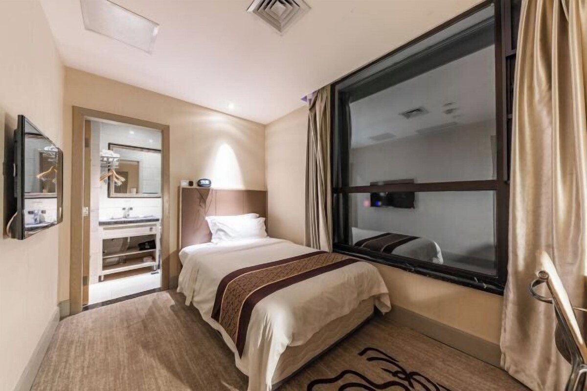 Une chambre d’hôtel avec un lit, une fenêtre, un miroir, une télévision et une salle de bain équipée d’un lavabo.