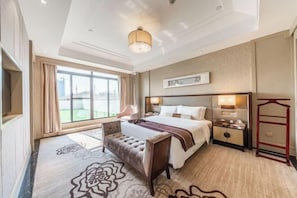Une chambre d’hôtel avec un grand lit, des tables de chevet, un banc, une grande fenêtre et une vue sur l’extérieur.