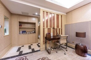 A hotel room with a desk, chair, lamp, and a minibar. - Xili International Hotel (Hong'an)