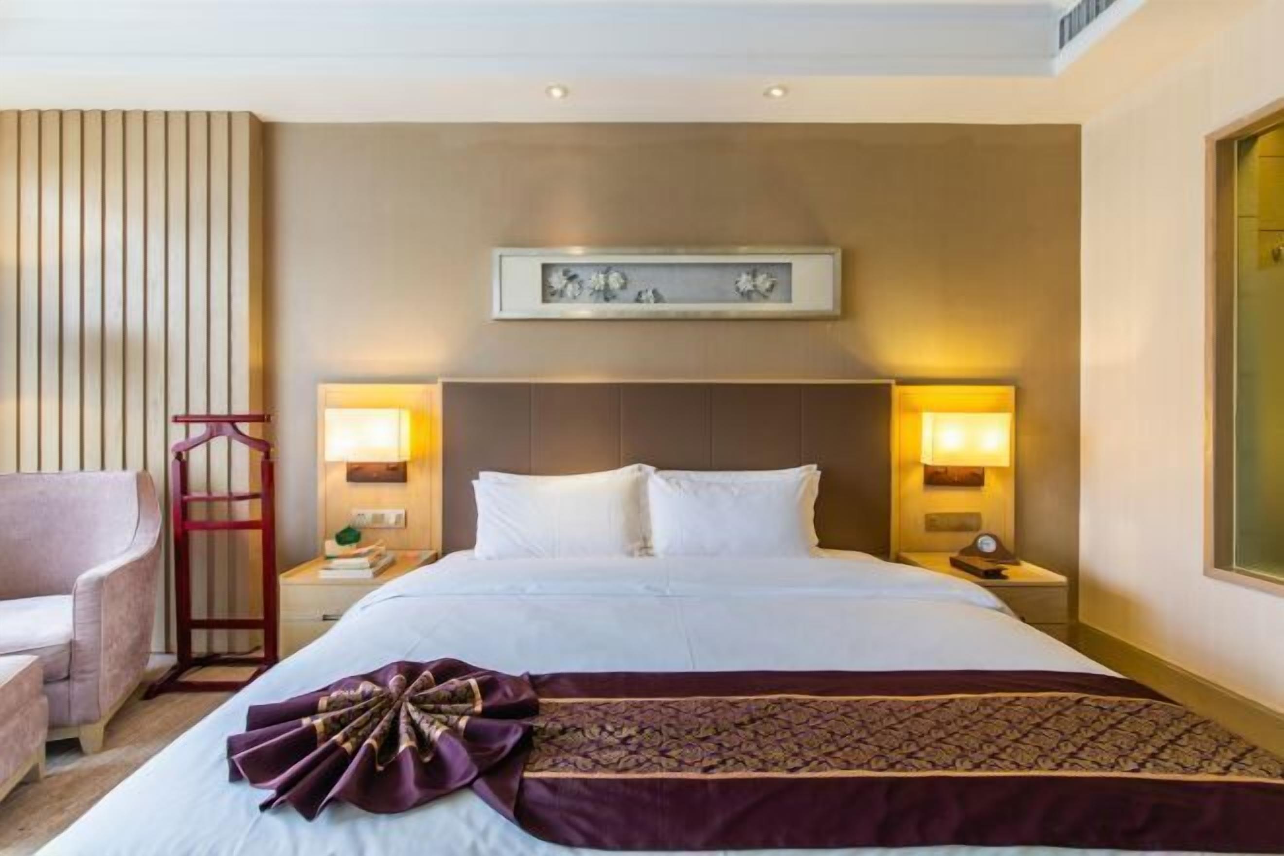 A hotel room with a bed, two bedside lamps, a nightstand, a chair, and a decorative wall piece.