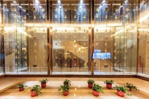 Un hall con un separador de vidrio que exhibe varios objetos, una escalera y plantas en macetas en el suelo.