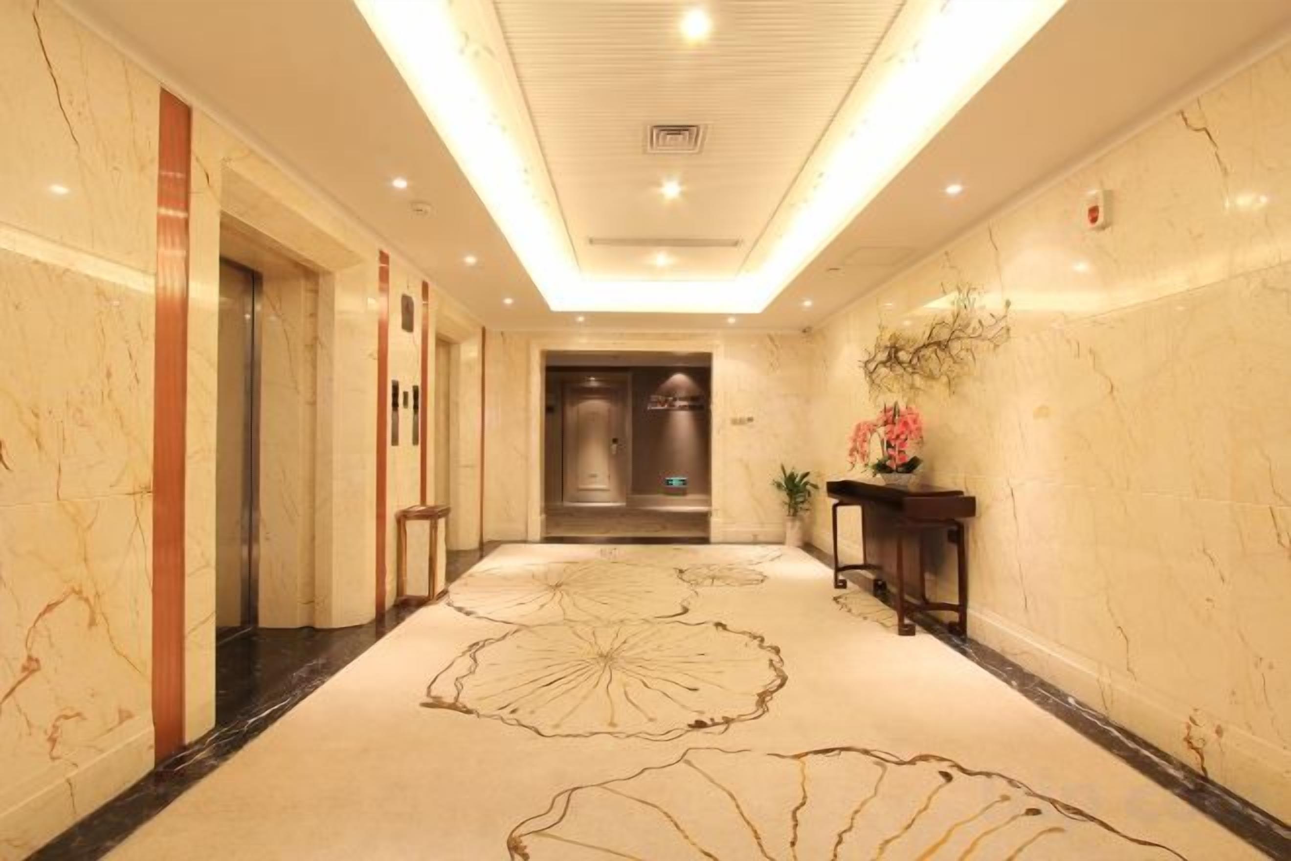 Pasillo de hotel con paredes de mármol, alfombra estampada y un ascensor.