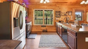 L’intérieur d’une cabane en bois comprend une cuisine équipée d’un réfrigérateur en acier inoxydable, de meubles de rangement en bois, d’une grande fenêtre et d’un coin repas.