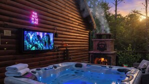 Une cabane en bois avec un bain à remous, une cheminée et un téléviseur diffusant un film.