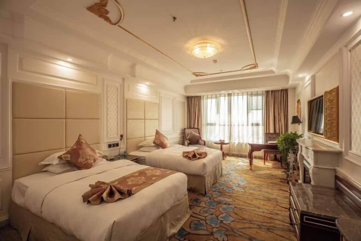 Habitación de hotel con dos camas, una zona de estar con una silla y una mesita, una chimenea y un ventanal grande con cortinas.