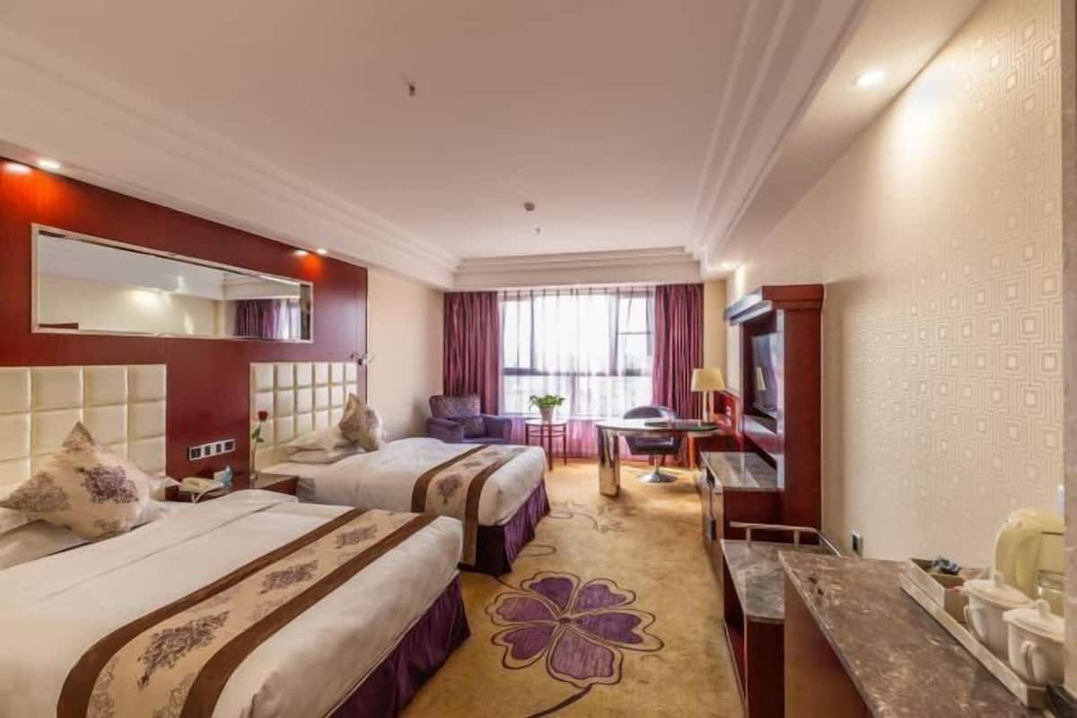 Habitación de hotel con dos camas, un escritorio, una silla, un televisor y un ventanal con cortinas.