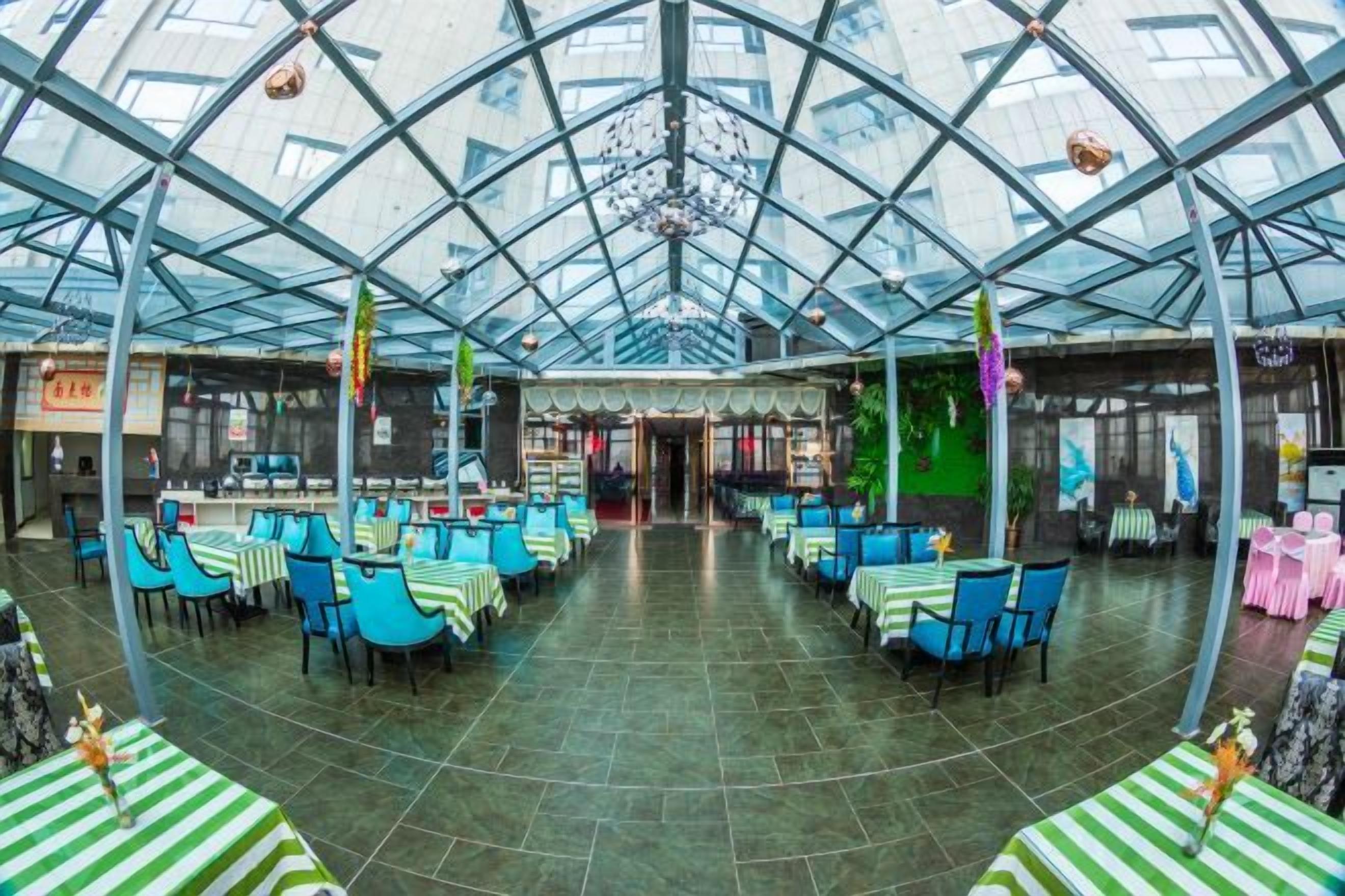 A spacious indoor area with a high ceiling and glass panels, featuring tables and chairs arranged for dining.
