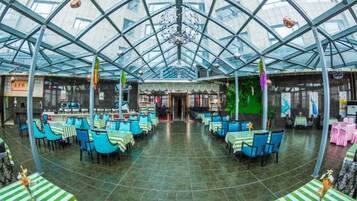 A spacious indoor area with a high ceiling and glass panels, featuring tables and chairs arranged for dining.