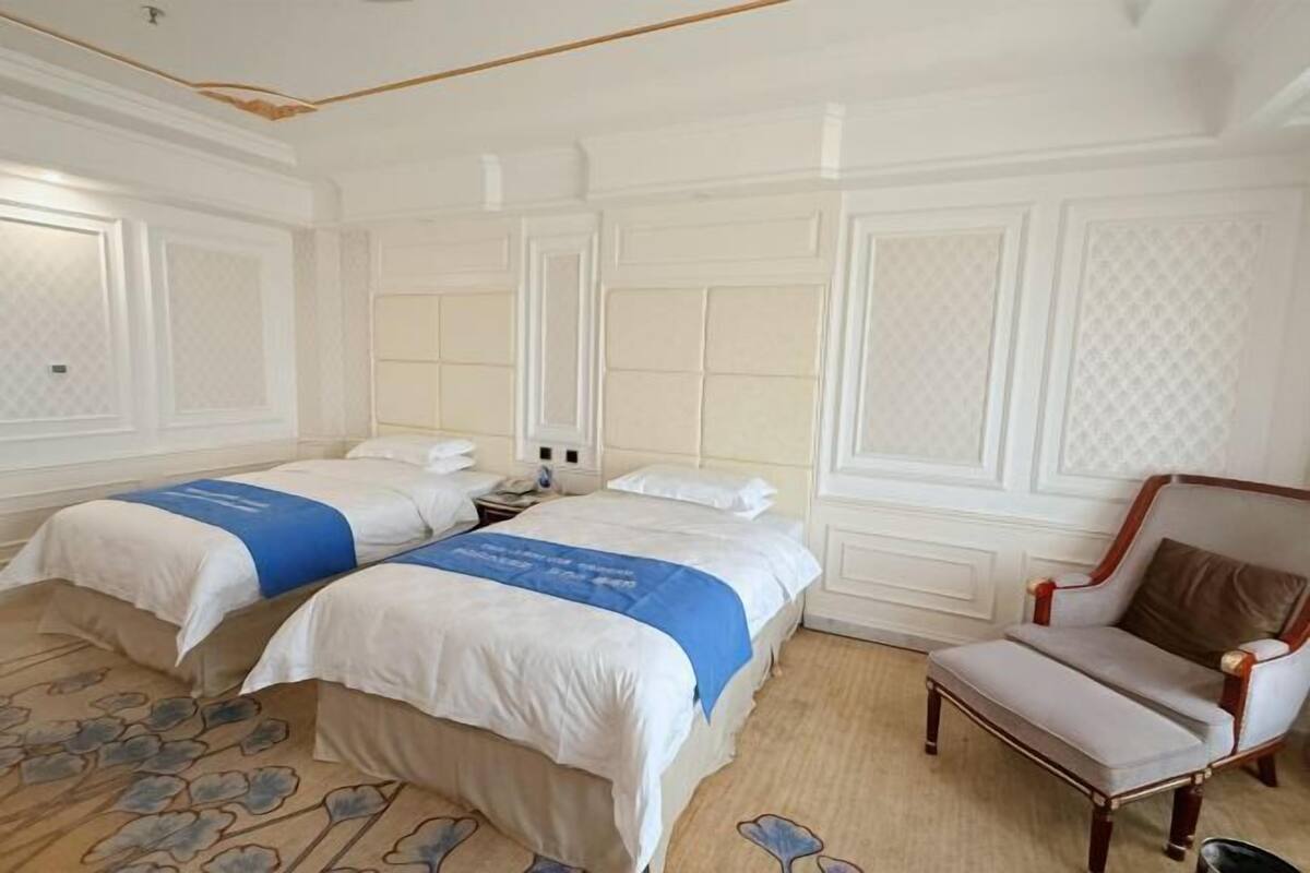 Habitación de hotel con dos camas, una silla y una alfombra estampada con motivos florales.