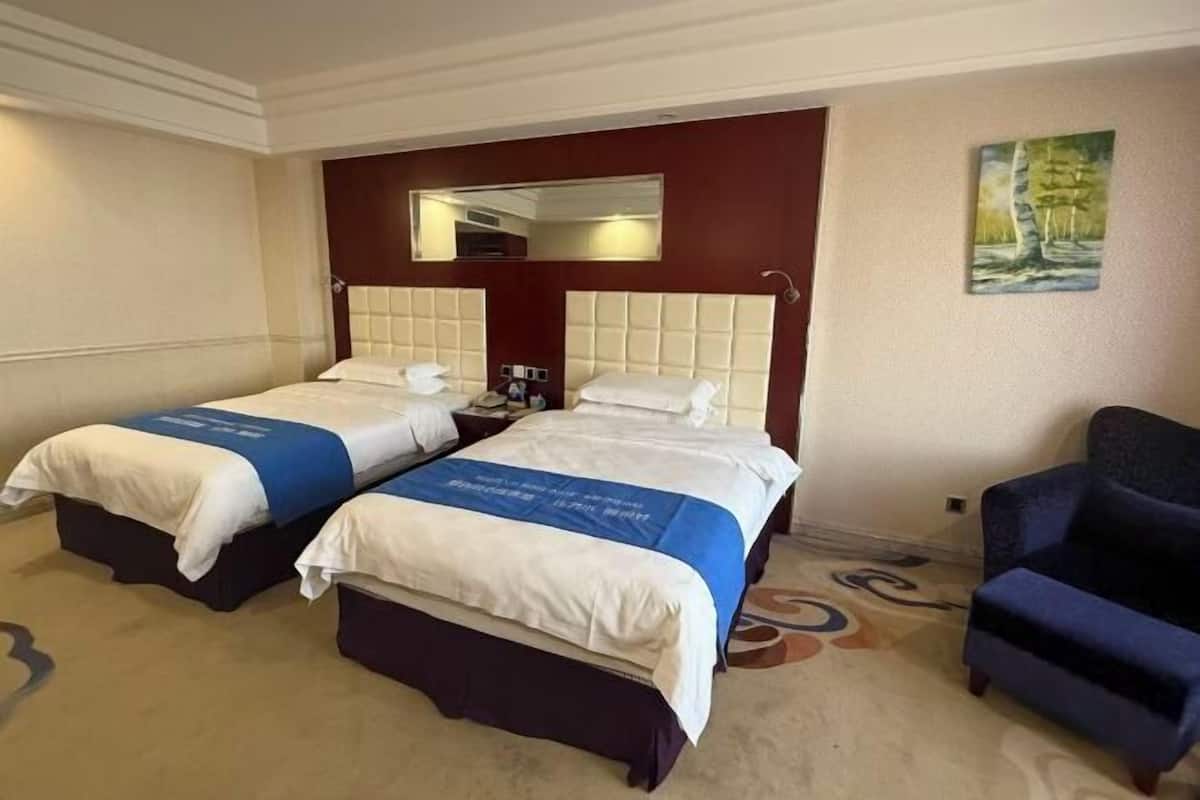 Habitación de hotel con dos camas, un espejo grande, un cuadro en la pared y un sillón azul.