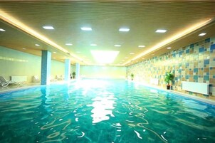 Una piscina interior con agua cristalina, rodeada de paredes con un diseño de azulejos y un techo con iluminación empotrada.