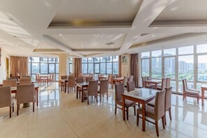 A spacious dining area with multiple tables and chairs, large windows, and a modern ceiling design.