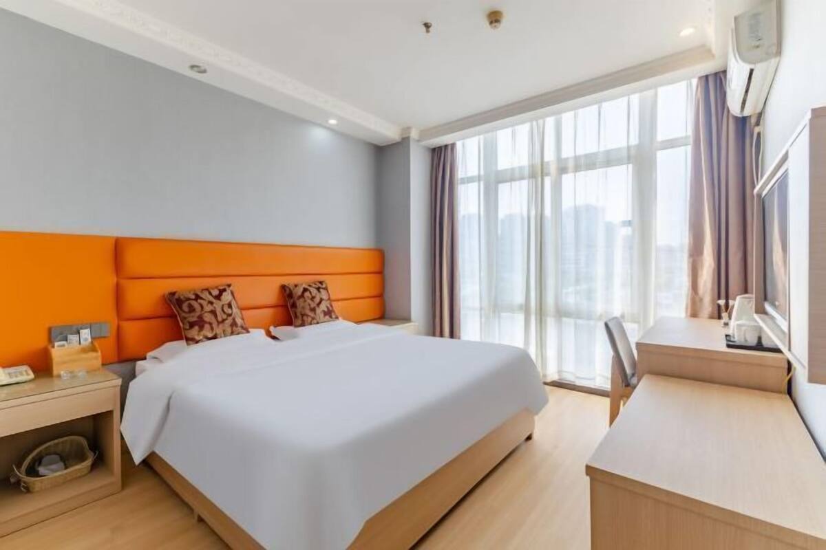 A hotel room with a bed, a desk, a chair, a nightstand, and a window with curtains.
