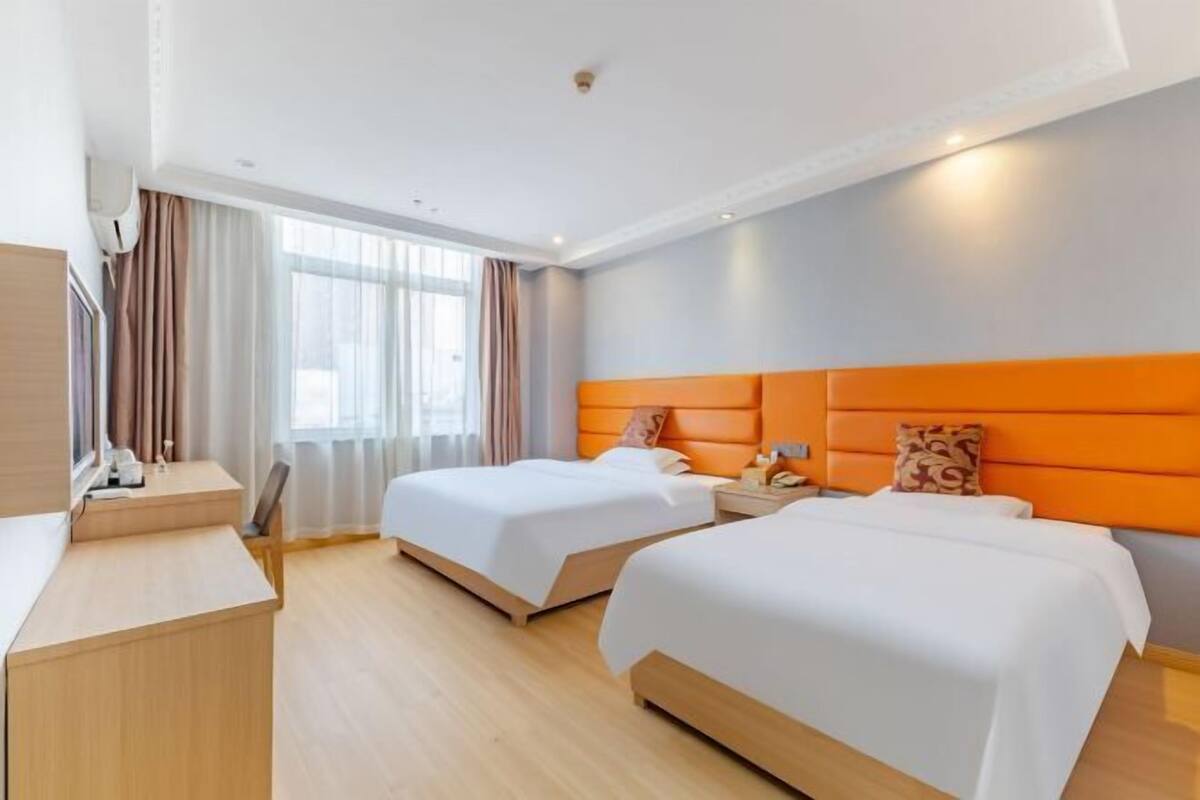 A hotel room with two beds, a desk, and a window with curtains.
