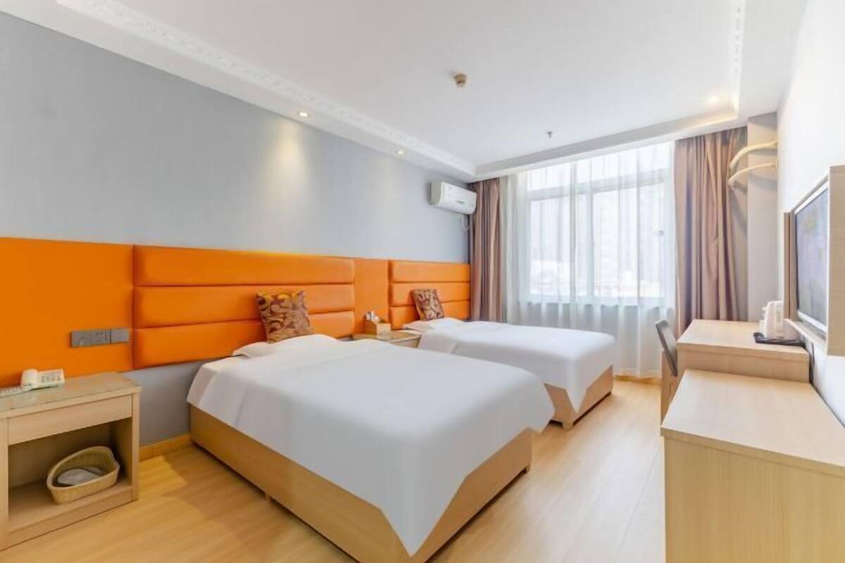 A hotel room with two beds, a desk, a chair, a TV, and a window with curtains.