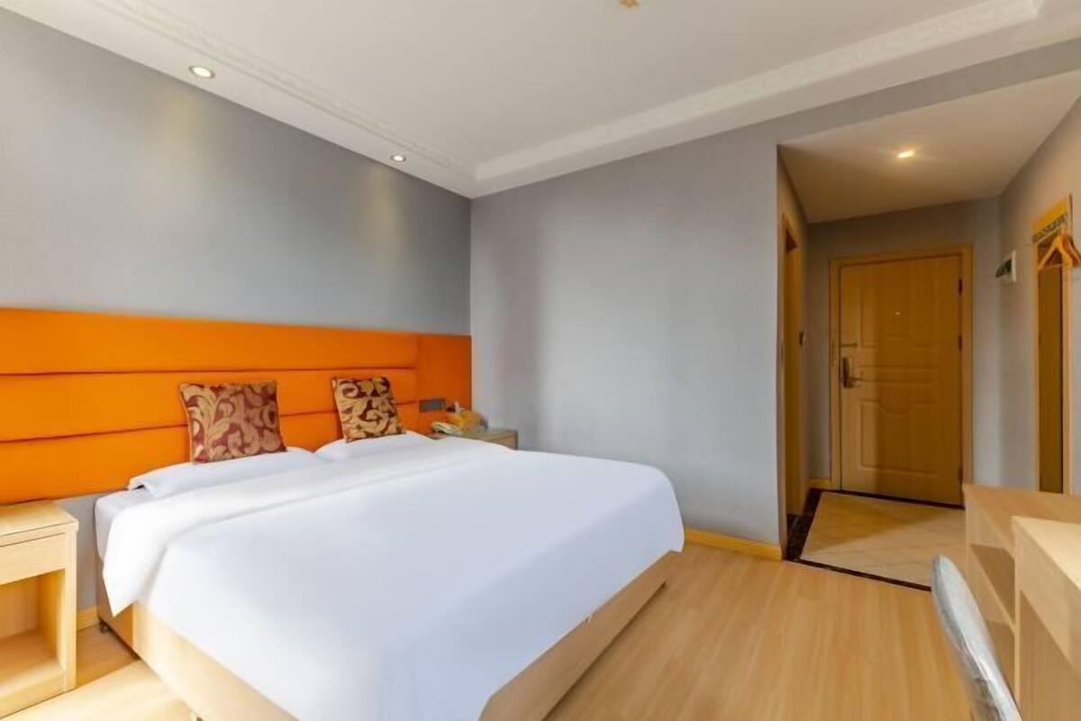 A hotel room with a large bed, a wooden headboard, a nightstand, and a door leading to another room.
