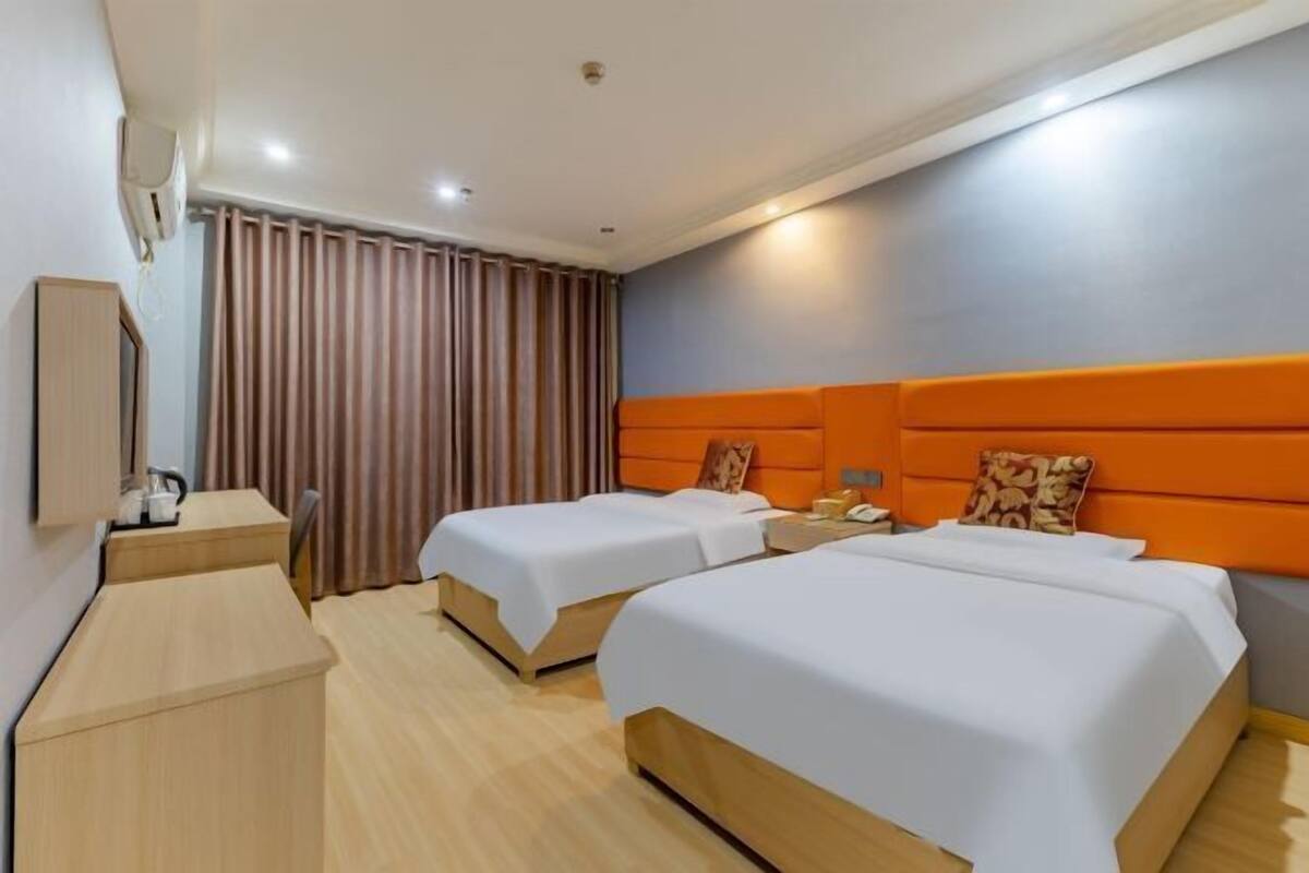 A hotel room with two beds, a desk, a chair, a nightstand, and a window with curtains.